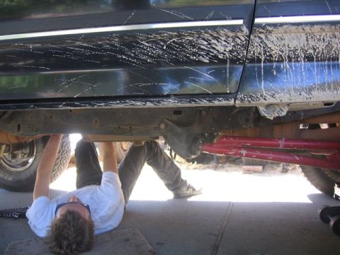 1989 Ford Bronco - A person works on the underside of a black SUV, revealing red suspension components.
