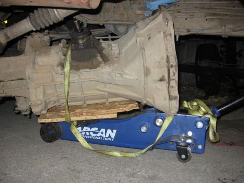 1989 Ford Bronco - A vehicle transmission is being supported by a blue hydraulic jack with straps and wooden planks.
