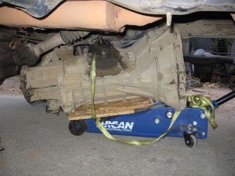 1989 Ford Bronco - A transmission is supported by a blue Arcan jack and straps during what appears to be a repair or upgrade.