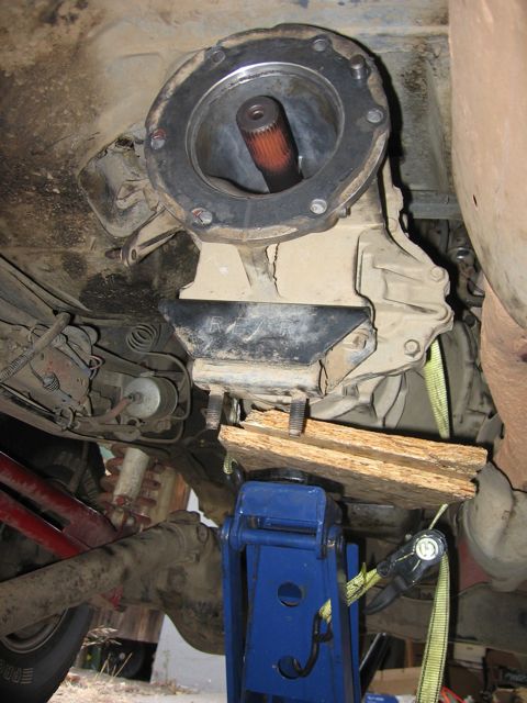 1989 Ford Bronco - Underside view of a vehicle's transmission and driveshaft assembly being supported by a jack and wood blocks during maintenance.