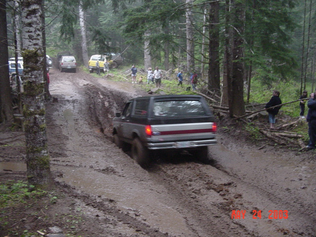 Dark Ford SUV with center brake light climbing a rutted muddy forest trail