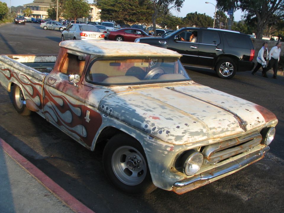 1957 Chevrolet pickup truck with custom flame paint and worn finish. Other vehicles and buildings in background