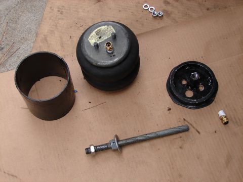 1973 Ford Ranchero - Disassembled air bag suspension components laid out on cardboard, including a convoluted (double-bellows) air spring with a warning label a…