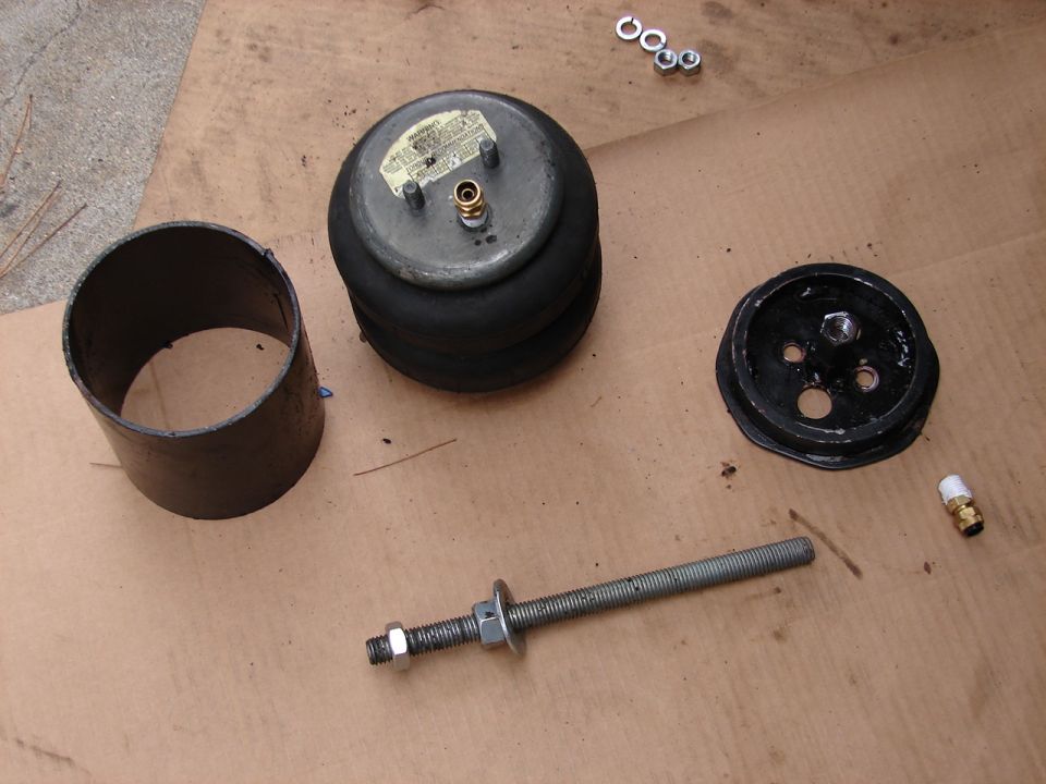 Air bag suspension parts on cardboard: air spring, steel sleeve, mounting plate, threaded rod, nuts, fittings.