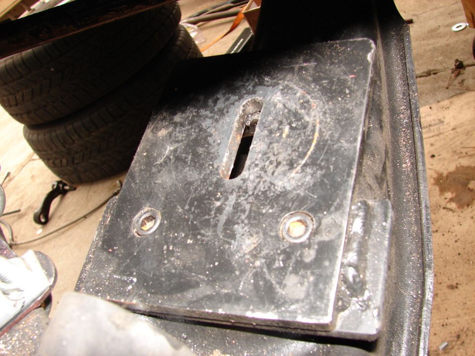 Fabricated black steel bracket plate with a center slot and two bolt holes on a shop floor
