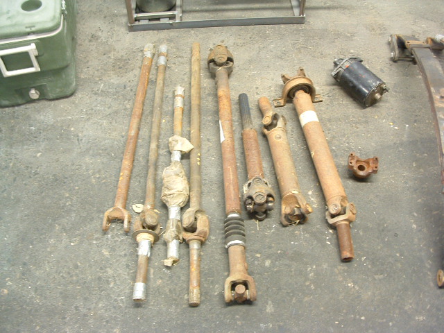 Several driveshafts and a black starter motor laid out on a concrete floor