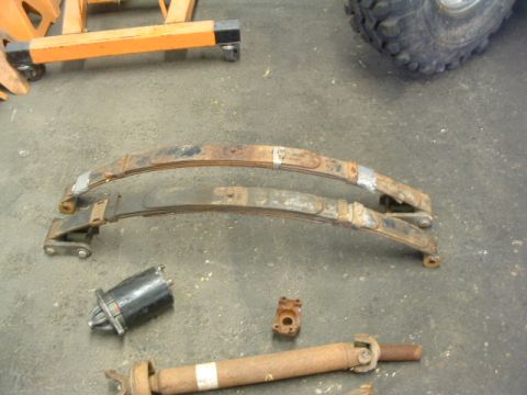 1994 Jeep YJ - Various automotive parts, including leaf springs and a driveshaft, are laid out on a workshop floor.