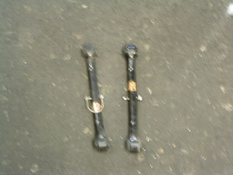 1994 Jeep YJ - Two black suspension control arms are shown against a textured gray surface.