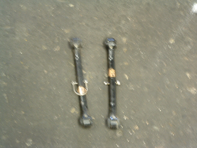 Two black metal suspension control arms with visible wear and a small gold-colored badge on one
