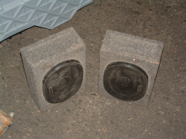 Two grey carpeted speaker boxes with black circular speakers, one on each