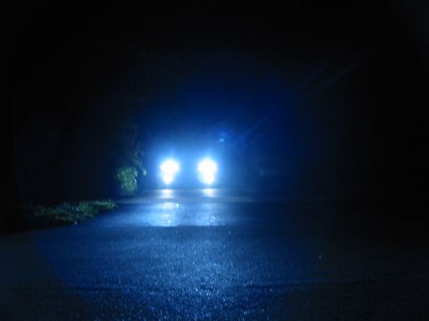 1995 Ford Thunderbird - Headlights pierce the darkness on a wet road, reflecting the bright blue light.