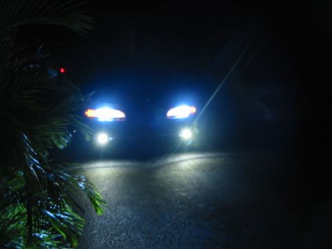 1995 Ford Thunderbird - A car's bright headlights cut through the darkness, illuminating the road ahead.