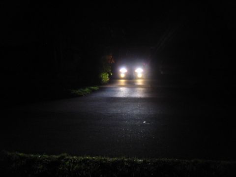 1995 Ford Thunderbird - Two vehicles approach on a dark road, their headlights illuminating the wet asphalt.