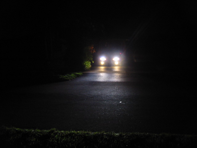 Two cars with headlights on drive down a dark, wet road at night