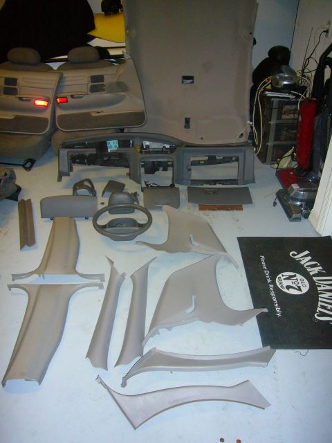 2000 Ford Crown Victoria - Various interior car parts are disassembled and laid out on the floor, including seats and trim panels.