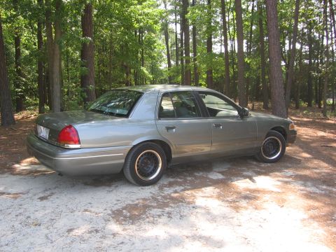2000 Ford Crown Victoria - A gray 2000 Ford Crown Victoria is parked on a dirt road surrounded by trees.