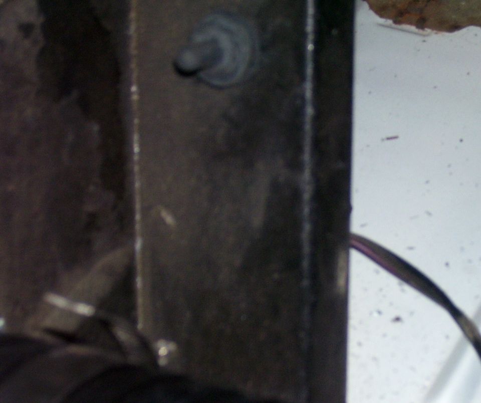 Close-up of a dark metal bracket with a stud and sealer beside a white painted panel