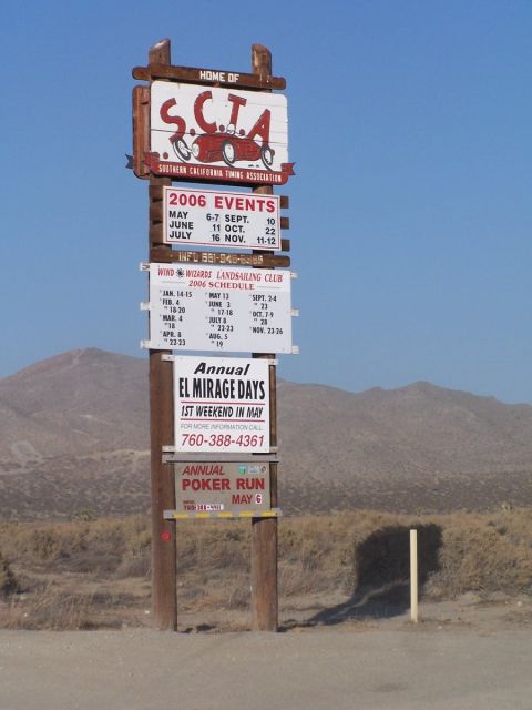 1990 Ford Bronco - Wooden roadside sign in the desert reading "HOME OF S.C.T.A. Southern California Timing Association" with a red lakester illustration, belo…