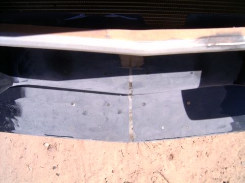 1978 Ford Mustang II - Close-up of a dark blue body panel laid on dirt with a wide strip sanded down to bare metal and a seam running through it, showing sanding…