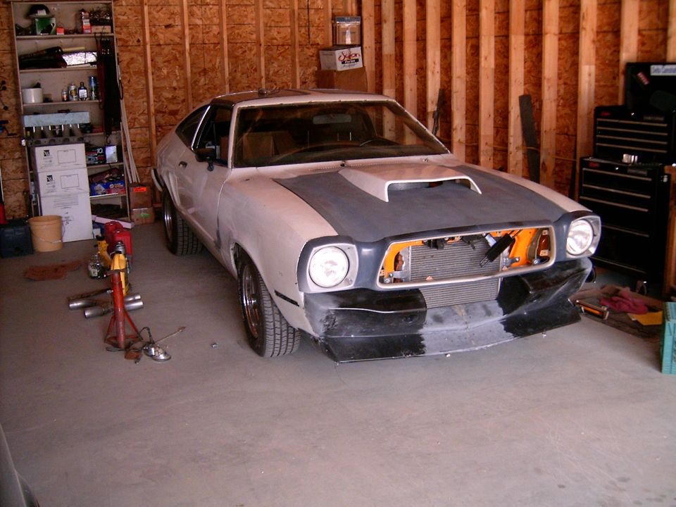Primered Mustang II hatchback project car in a garage with hood scoop and open grille area