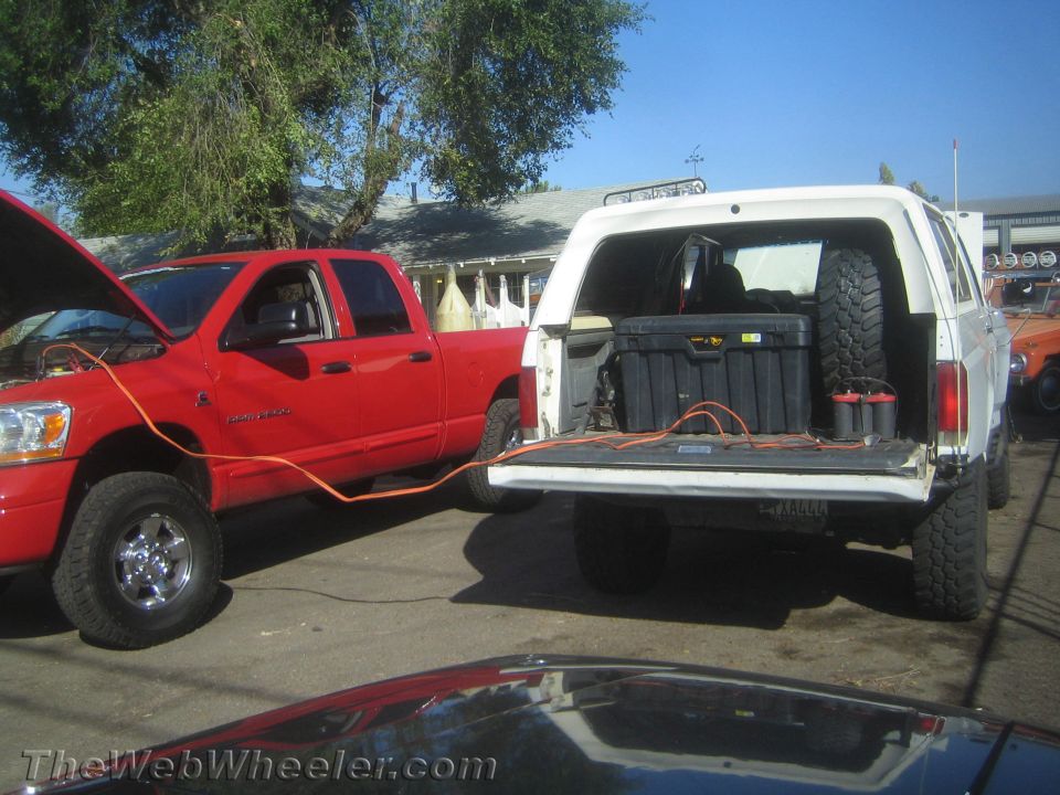 Red Dodge truck jump-starting a white SUV with open tailgate in a parking lot