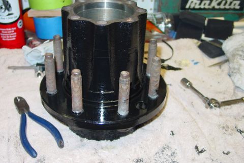 1993 Ford Bronco - A black wheel hub assembly with studs, pliers, and a socket wrench are on a workbench.
