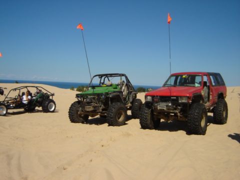 1992 Ford Bronco - Multiple off-road vehicles are parked on sand dunes under a clear blue sky.