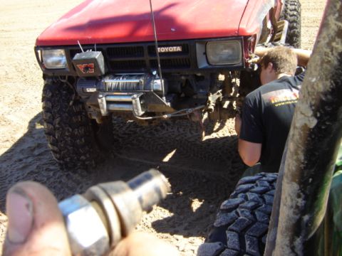 1992 Ford Bronco - A person works on a red Toyota truck equipped with a winch, stuck in sandy terrain.