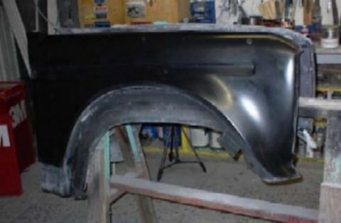 1986 Ford Bronco - A black front fender panel for a truck or SUV rests on wooden sawhorses in a workshop, showing the wheel arch and a body character line wit…