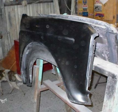 1986 Ford Bronco - A vehicle fender part is shown on a stand, with a dog in the background.