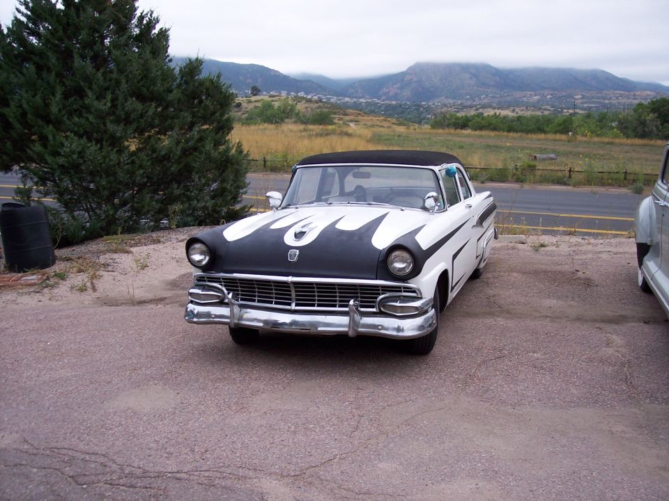 White and black Ford Fairlane Crown Victoria with flame decals on the hood, parked outside with mountains in the background
