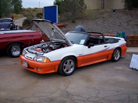 1972 Ford Ranchero - A white and orange 1990 Ford Mustang GT convertible is displayed with its hood open, parked beside a red pickup truck.