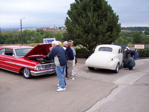 1972 Ford Ranchero - Two classic cars are on display outdoors, with people gathered around the red one.