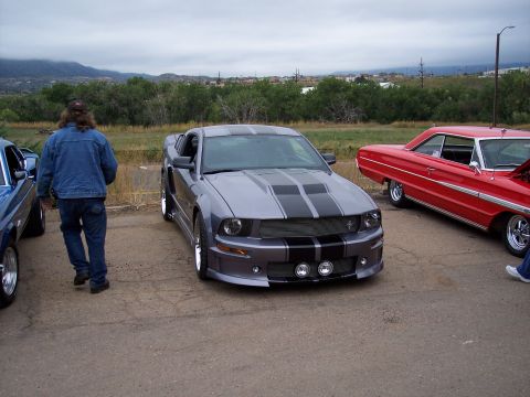 1972 Ford Ranchero - A modern Ford Mustang is parked next to a vintage red car, with a person walking away from the camera.