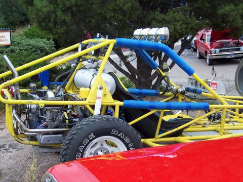 1972 Ford Ranchero - A custom dune buggy with a prominent engine and roll cage is parked next to a red car.