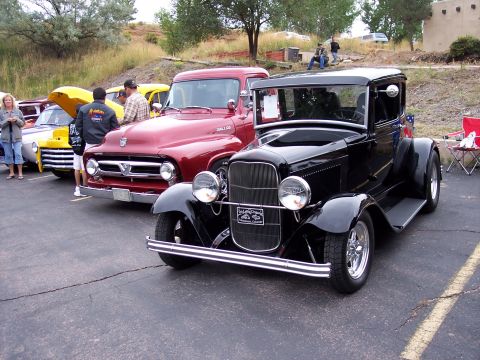 1972 Ford Ranchero - A black hot rod coupe is parked next to a red pickup truck at an outdoor event.