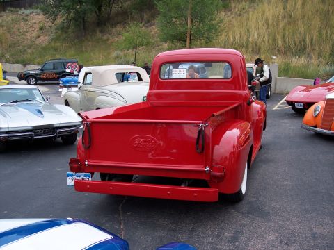 1972 Ford Ranchero - Rear view of a bright red 1950 Ford pickup truck, a "For Sale" sign in the rear window and other classic cars nearby.