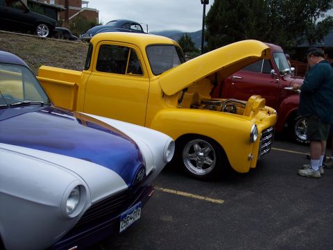 1972 Ford Ranchero - A yellow 1950s pickup truck is displayed with its hood open, parked alongside other vehicles.