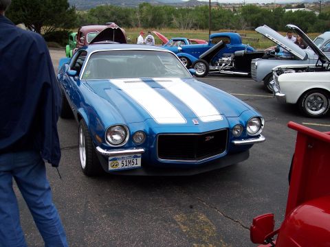 1972 Ford Ranchero - A blue 1970 Chevrolet Camaro with white racing stripes is parked at an outdoor car show.