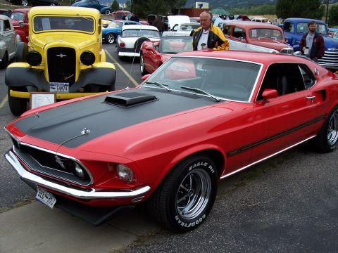 1972 Ford Ranchero - A classic red muscle car is parked next to a yellow vintage truck at an outdoor car show.