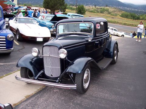 1972 Ford Ranchero - A dark blue 1932 Ford coupe hot rod is parked at a car show with other vehicles in the background.