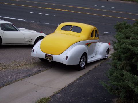 1972 Ford Ranchero - A two-tone yellow and white hot rod coupe is parked next to a white Corvette.