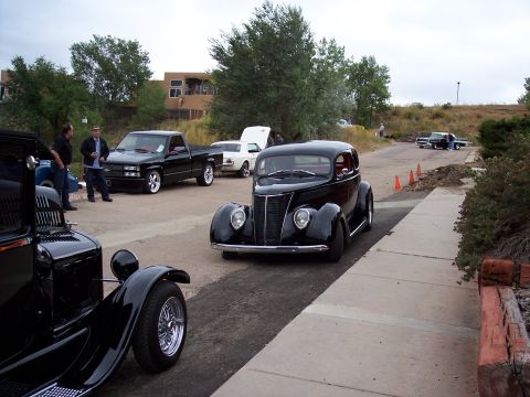 1972 Ford Ranchero - A black 1937 Ford hot rod sedan is parked on a street with other vehicles present.