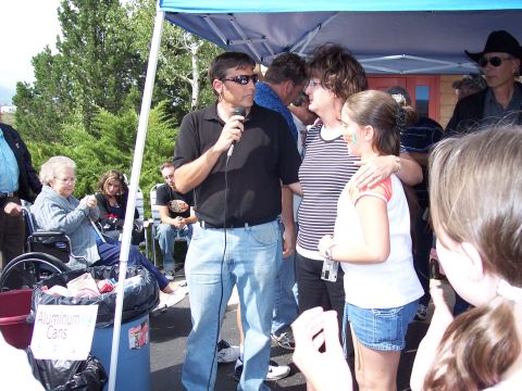 1972 Ford Ranchero - A group of people are gathered under a blue tent, with one man holding a microphone and speaking to the crowd.
