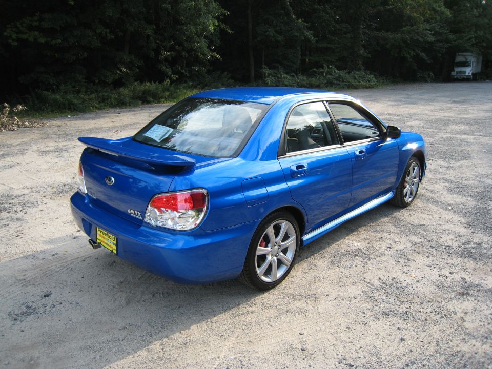 Blue Subaru WRX sedan parked on a gravel lot with trees in the background