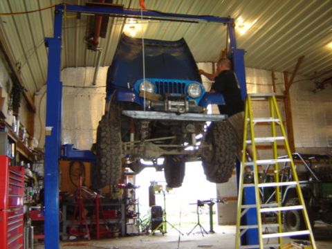 1992 Ford Bronco - A blue Jeep is being worked on while elevated on a garage lift.