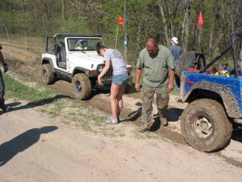1992 Ford Bronco - Two off-road vehicles are stuck in the mud on a trail, with people standing around them.
