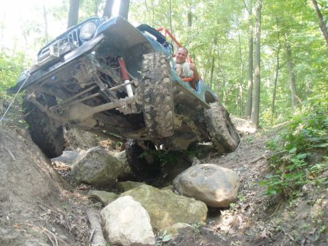 1992 Ford Bronco - A modified off-road vehicle is shown navigating a challenging rocky terrain in a wooded area.
