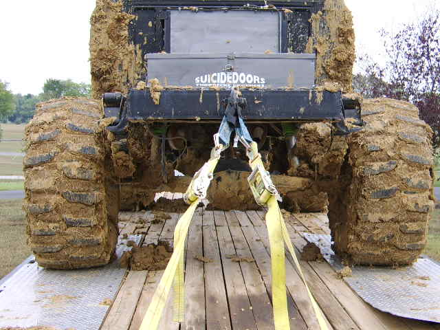 Mud-covered truck rear with large tires, being towed on a trailer