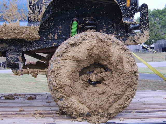 Mud-covered truck tire and suspension components, including a green shock absorber